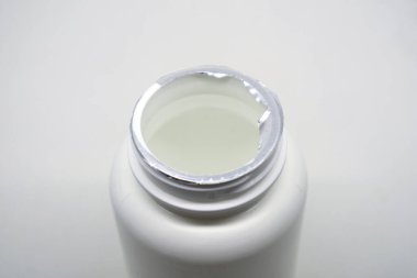 An open white bottle against a white background, viewed from above, highlighting the torn foil seal.