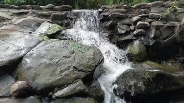 Close-up footage of a small waterfall cascading over mossy rocks. Perfect nature background for relaxation and meditation projects.