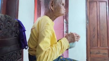 Side profile of a wrinkled grandma in simple attire, eating slowly. Captures the reality of an elderly person's daily life. Good for lifestyle and health projects on aging.