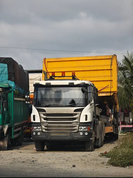 İnşaat alanında park etmiş parlak sarı bir konteynırı olan ağır bir çöp kamyonu.