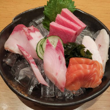 Ezilmiş buz üzerinde taze kutoro, somon ve hamachi dilimleri ile güzel bir Japon saşimi tabağı. Shiso yaprağı ve deniz yosunuyla karanlık bir kasede servis edilmiş.