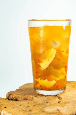Refreshing tropical fruit pickle featuring sliced young mango, bilimbi, and longan in sweet-sour brine, displayed in a glass over rustic wood with minimalist white background.