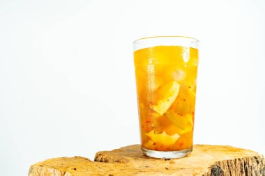 Refreshing tropical fruit pickle featuring sliced young mango, bilimbi, and longan in sweet-sour brine, displayed in a glass over rustic wood with minimalist white background.