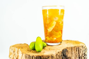 Refreshing tropical fruit pickle featuring sliced young mango, bilimbi, and longan in sweet-sour brine, displayed in a glass over rustic wood with minimalist white background.