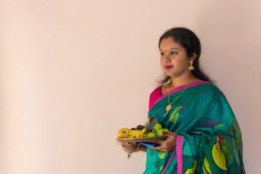 A beautiful Indian Bengali woman in green traditional ethnic saree holding puja thali or prayer plate on white background. Selective focus.