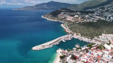 Stunning aerial view of Kalkan, Turkeys picturesque bay. White Mediterranean houses and luxury villas descend to the sunny marina with yachts. Crystal-turquoise waters and islands in the distance. Perfect for travel, resort projects. 4K 60 fps.