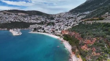 Stunning aerial view of Kalkan, Turkeys picturesque bay. White Mediterranean houses and luxury villas descend to the sunny marina with yachts. Crystal-turquoise waters and islands in the distance. Perfect for travel, resort projects. 4K 60 fps.