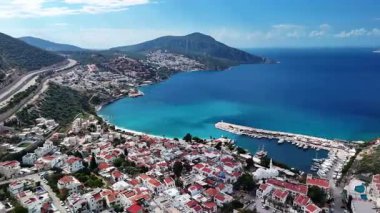 Stunning aerial view of Kalkan, Turkeys picturesque bay. White Mediterranean houses and luxury villas descend to the sunny marina with yachts. Crystal-turquoise waters and islands in the distance. Perfect for travel, resort projects. 4K 60 fps.