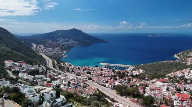 Stunning aerial view of Kalkan, Turkeys picturesque bay. White Mediterranean houses and luxury villas descend to the sunny marina with yachts. Crystal-turquoise waters and islands in the distance. Perfect for travel, resort projects. 4K 60 fps.