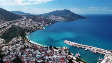 Stunning aerial view of Kalkan, Turkeys picturesque bay. White Mediterranean houses and luxury villas descend to the sunny marina with yachts. Crystal-turquoise waters and islands in the distance. Perfect for travel, resort projects. 4K 60 fps.