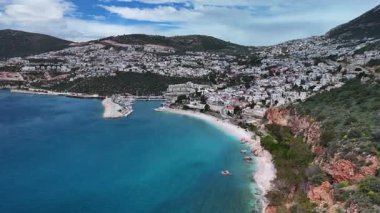 Stunning aerial view of Kalkan, Turkeys picturesque bay. White Mediterranean houses and luxury villas descend to the sunny marina with yachts. Crystal-turquoise waters and islands in the distance. Perfect for travel, resort projects. 4K 60 fps.