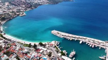 Stunning aerial view of Kalkan, Turkeys picturesque bay. White Mediterranean houses and luxury villas descend to the sunny marina with yachts. Crystal-turquoise waters and islands in the distance. Perfect for travel, resort projects. 4K 60 fps.