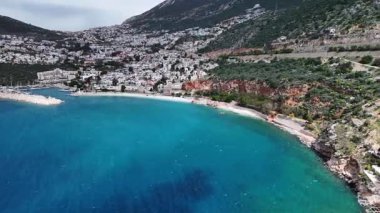 Stunning aerial view of Kalkan, Turkeys picturesque bay. White Mediterranean houses and luxury villas descend to the sunny marina with yachts. Crystal-turquoise waters and islands in the distance. Perfect for travel, resort projects. 4K 60 fps.
