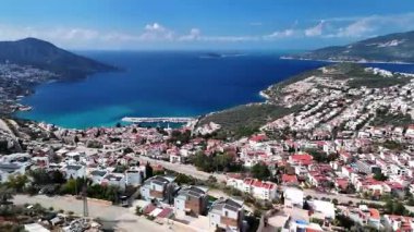 Stunning aerial view of Kalkan, Turkeys picturesque bay. White Mediterranean houses and luxury villas descend to the sunny marina with yachts. Crystal-turquoise waters and islands in the distance. Perfect for travel, resort projects. 4K 60 fps.
