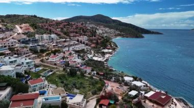 Stunning aerial view of Kalkan, Turkeys picturesque bay. White Mediterranean houses and luxury villas descend to the sunny marina with yachts. Crystal-turquoise waters and islands in the distance. Perfect for travel, resort projects. 4K 60 fps.