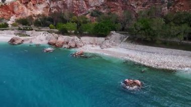 Türkiye 'nin Kalkan kentinde kıyı şeridi boyunca deniz kenarındaki gezinti ve yürüyüş yolunun havadan görüntüsü. Kızıl kayalıklar, yeşil tepeler ve turkuaz deniz manzaralı bir Akdeniz manzarası oluşturur