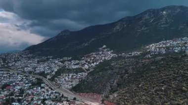 Türkiye 'nin Kalkan kentinin panoramik manzarası. Dağların eteklerindeki beyaz evler bulutlu bir gökyüzünün altında. Manzaralı Akdeniz kıyı manzarası.