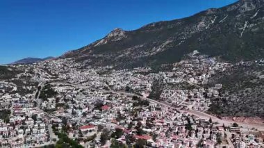 Kalkan, Türkiye 'nin havadan 4K görüntüsü. İnsansız hava aracı dağın manzarasını yakalıyor ve tepe boyunca yeşil ve deniz manzaralı zarif beyaz villalar inşa ediliyor.