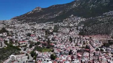 Kalkan, Türkiye 'nin havadan 4K görüntüsü. İnsansız hava aracı dağın manzarasını yakalıyor ve tepe boyunca yeşil ve deniz manzaralı zarif beyaz villalar inşa ediliyor.