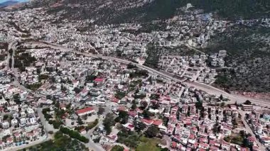 Kalkan, Türkiye 'nin havadan 4K görüntüsü. İnsansız hava aracı dağın manzarasını yakalıyor ve tepe boyunca yeşil ve deniz manzaralı zarif beyaz villalar inşa ediliyor.