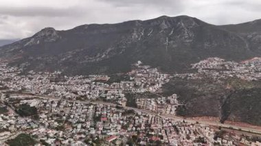 Kalkan, Türkiye 'nin havadan 4K görüntüsü. İnsansız hava aracı dağın manzarasını yakalıyor ve tepe boyunca yeşil ve deniz manzaralı zarif beyaz villalar inşa ediliyor.