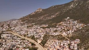 Kalkan, Türkiye 'nin havadan 4K görüntüsü. İnsansız hava aracı dağın manzarasını yakalıyor ve tepe boyunca yeşil ve deniz manzaralı zarif beyaz villalar inşa ediliyor.