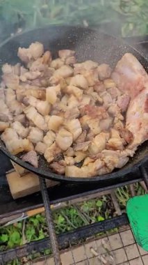 Sizzling pork belly in a pan over a campfire, cooking crispy outdoors, savoring the rich flavors of a delicious meal in the wilderness, camping feast, grilling food, picnic delight, cooking.