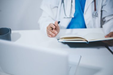 Doktorun odasında dizüstü bilgisayarla çalışan orta yaşlı bir kadın doktor.