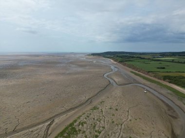 The wide expanse of sand stretches to the horizon, revealing a winding river. Green fields are visible in the background beneath a cloudy sky, showcasing natures beauty.