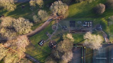 Aerial view showcases a childrens playground and park with various play structures, surrounded by trees and pathways. Sunlight filters through the branches, creating a serene atmosphere.