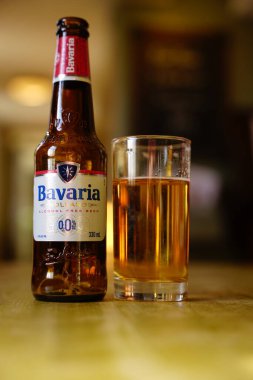 A bottle of Bavaria sits next to a glass filled with sparkling golden beverage. Soft lighting highlights the bottles label and the rich color of the drink. This scene captures a moment of relaxation.