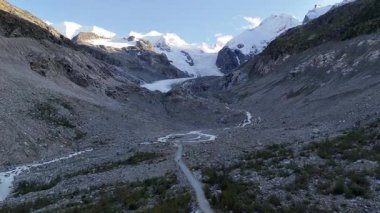 İsviçre 'nin Engadin Vadisi' ndeki Morteratsch Buzulu 'ndan yükselen buzul nehrinin manzarası. Fotoğraf, karla kaplı zirveleri, kayaları ve mavi buzul suyuyla dramatik alp manzarasını gösteriyor. Seyahat, turizm ve çevre için mükemmel.