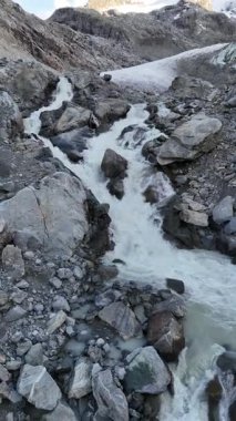 İsviçre 'nin Engadin Vadisi' ndeki Morteratsch Buzulu 'ndan yükselen buzul nehrinin manzarası. Fotoğraf, karla kaplı zirveleri, kayaları ve mavi buzul suyuyla dramatik alp manzarasını gösteriyor. Seyahat, turizm ve çevre için mükemmel.