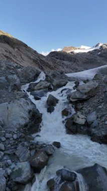 İsviçre 'nin Engadin Vadisi' ndeki Morteratsch Buzulu 'ndan yükselen buzul nehrinin manzarası. Fotoğraf, karla kaplı zirveleri, kayaları ve mavi buzul suyuyla dramatik alp manzarasını gösteriyor. Seyahat, turizm ve çevre için mükemmel.