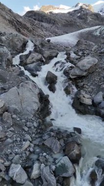 İsviçre 'nin Engadin Vadisi' ndeki Morteratsch Buzulu 'ndan yükselen buzul nehrinin manzarası. Fotoğraf, karla kaplı zirveleri, kayaları ve mavi buzul suyuyla dramatik alp manzarasını gösteriyor. Seyahat, turizm ve çevre için mükemmel.