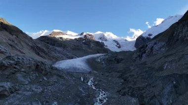 İsviçre 'nin Engadin Vadisi' ndeki Morteratsch Buzulu 'ndan yükselen buzul nehrinin manzarası. Fotoğraf, karla kaplı zirveleri, kayaları ve mavi buzul suyuyla dramatik alp manzarasını gösteriyor. Seyahat, turizm ve çevre için mükemmel.