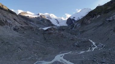 İsviçre 'nin Engadin Vadisi' ndeki Morteratsch Buzulu 'ndan yükselen buzul nehrinin manzarası. Fotoğraf, karla kaplı zirveleri, kayaları ve mavi buzul suyuyla dramatik alp manzarasını gösteriyor. Seyahat, turizm ve çevre için mükemmel.