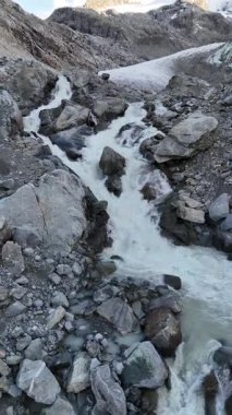 İsviçre 'nin Engadin Vadisi' ndeki Morteratsch Buzulu 'ndan yükselen buzul nehrinin manzarası. Fotoğraf, karla kaplı zirveleri, kayaları ve mavi buzul suyuyla dramatik alp manzarasını gösteriyor. Seyahat, turizm ve çevre için mükemmel.