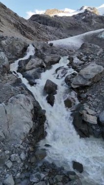 İsviçre 'nin Engadin Vadisi' ndeki Morteratsch Buzulu 'ndan yükselen buzul nehrinin manzarası. Fotoğraf, karla kaplı zirveleri, kayaları ve mavi buzul suyuyla dramatik alp manzarasını gösteriyor. Seyahat, turizm ve çevre için mükemmel.