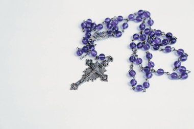 Beyaz arka planda gümüş haç ve mor boncuklu tespih yatıyordu. Tespih kısmen sarılmış ve haç İsa 'nın bir tasvirini sergiliyor..