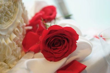 Koyu kırmızı bir gül, bir düğün pastasının yanına romantik bir dokunuş ekler. Zarif masa dekorunun bir parçası.