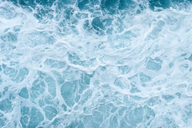 Canlı turkuaz okyanus dalgalarının hava görüntüsü karmaşık köpük desenleri yaratarak deniz suyunun dinamik dokusunu resmediyor.