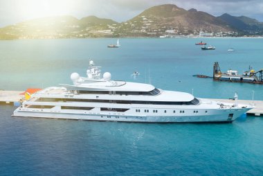 Arkasında manzaralı tepeler olan, berrak Karayip sularına yanaşmış lüks bir yat.