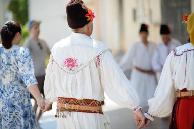 Vardim, Bulgaristan - 07 / 27 / 2024: Bulgaristan 'ın Vratsa bölgesindeki Sofronievo kentinde düzenlenen bir dans sırasında el ele tutuşurken ayrıntılı nakış, dekoratif kemer ve kültürel giysiler sergilenen geleneksel Ulah kıyafetli bir erkek dansçının yakın çekimi.