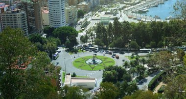 Malaga 'daki Plaza de la Marina' nın hava manzarasında İspanya 'nın göbeğinde palmiye ağaçlarıyla çevrili bir çeşme ve güneşli bir günde tekneli bir liman var..