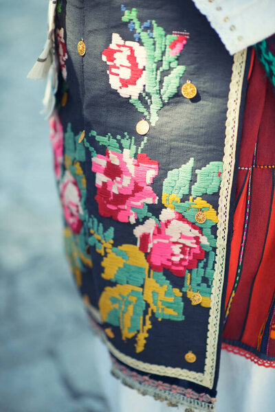 Exquisitely crafted apron featuring vibrant floral embroidery and golden coin embellishments on dark fabric, showcasing timeless artisanship.