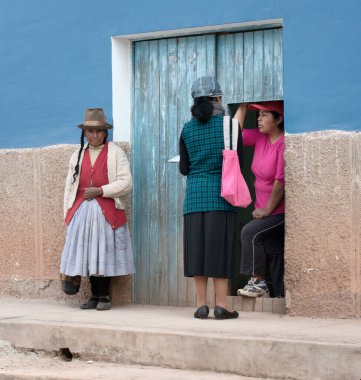 07 / 26 / 2018 - Maras, Peru: Peru 'nun Maras kentinde geleneksel bir evin önünde sohbet eden kadınların yer aldığı samimi bir sahne. Görüntü, geleneksel Peru kıyafetleri içinde duvara yaslanmış bir kadının kültür atmosferini yakalıyor.