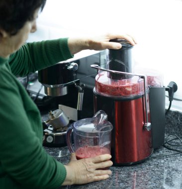 Kıdemli kadın meyve ve sebzelerden taze meyve suyu yapmak için meyve sıkacağı kullanıyor.