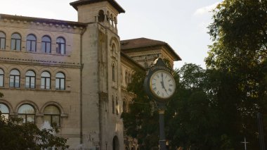Bükreş, Romanya - 09 / 21 / 2025: Bükreş Tarihi Üniversitesi binası ve Bükreş şehir merkezindeki tarihi akademik mimariyi gösteren üniversite saati öğleden sonra saatinde ele geçirildi