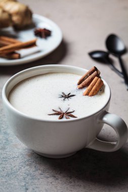 Beyaz fincanda tarçın, zencefil ve yıldız anasonlu ev yapımı Chai latte, yakın plan, koyu arka plan..